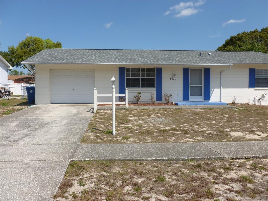 A single-story white house features a garage, blue shutters, and a concrete driveway — 5330 SPRINGWOOD ROAD, SPRING HILL, FL