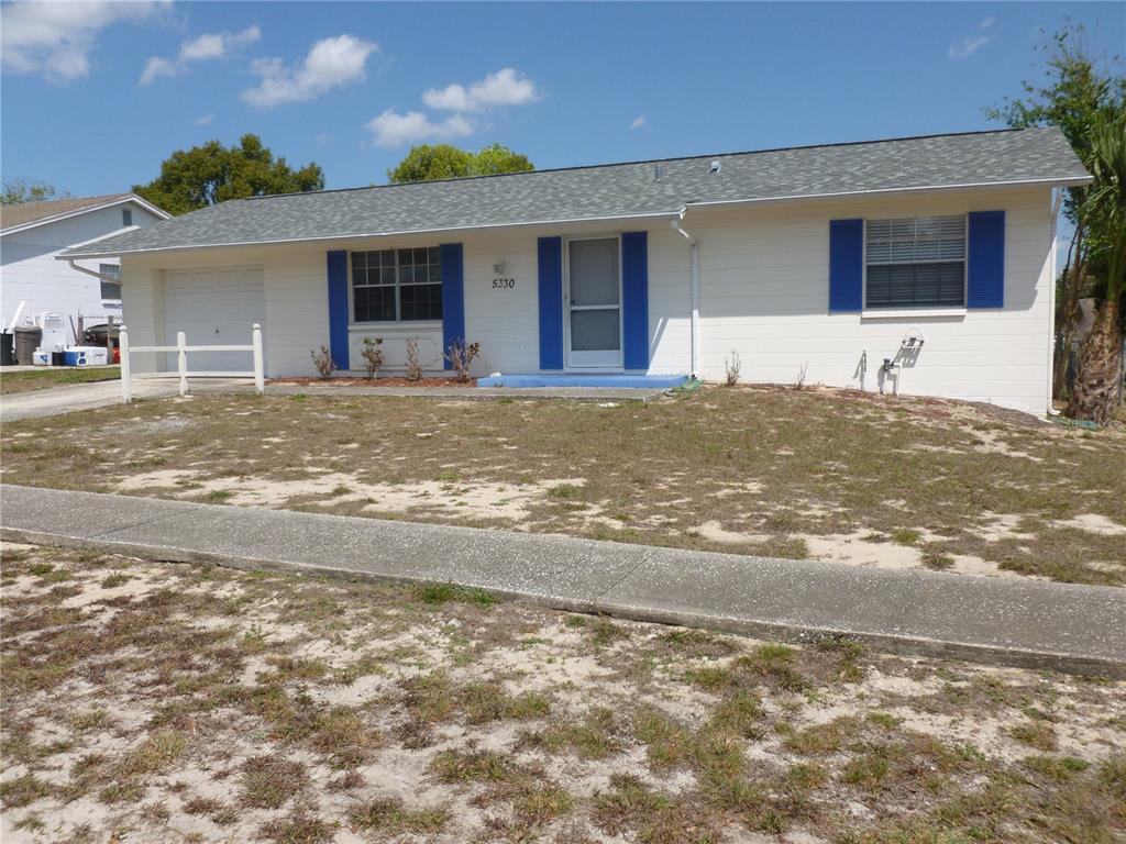 A single-story house with white siding, blue shutters, and a front lawn — 5330 SPRINGWOOD ROAD, SPRING HILL, FL