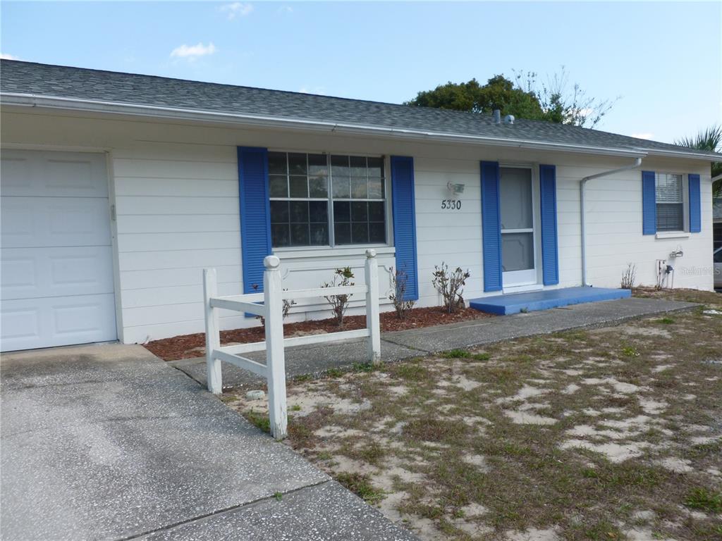 A single-story house with white siding, blue shutters, a garage, and a small front yard — 5330 SPRINGWOOD ROAD, SPRING HILL, FL
