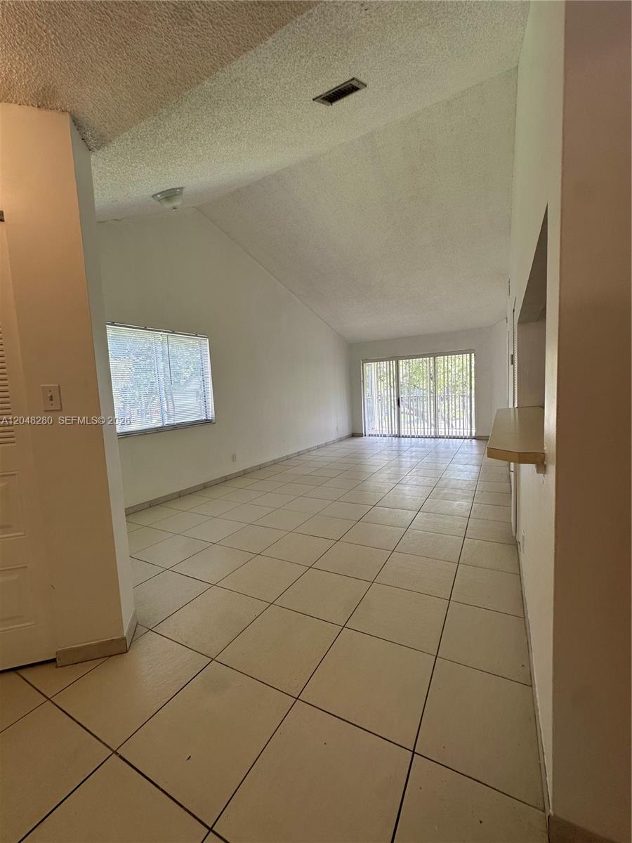An empty living room features white tile flooring, a vaulted ceiling, and sliding glass doors — MIAMI, FL
