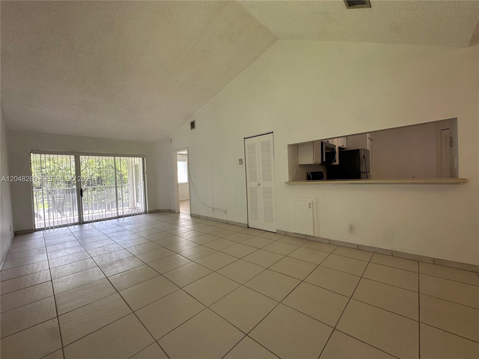 An open living area features vaulted ceilings, light tile flooring, and a kitchen pass-through window — MIAMI, FL