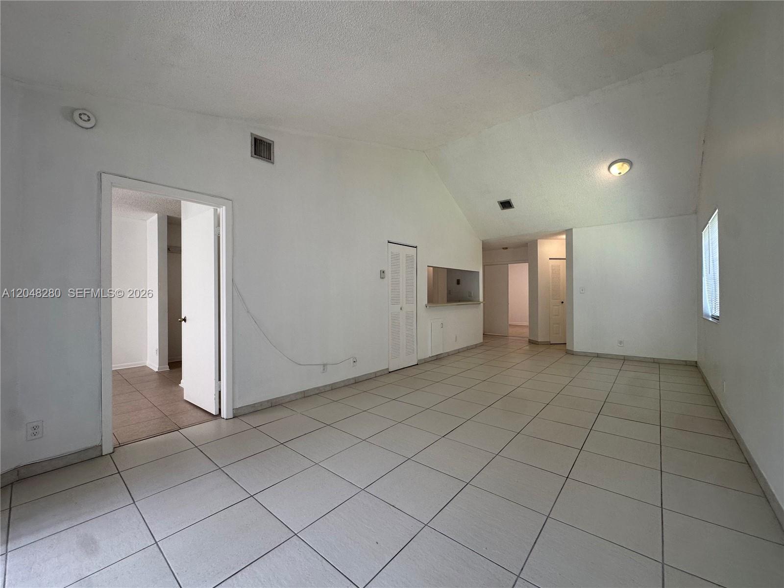 An empty room features white walls, vaulted ceilings, and light-colored tiled flooring — MIAMI, FL