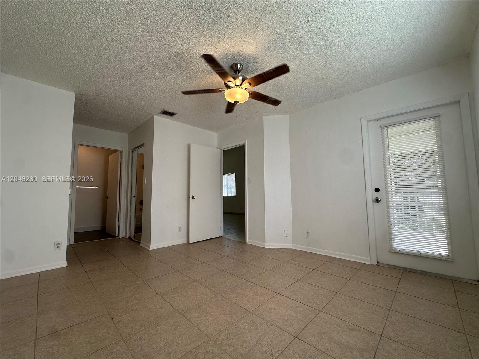 An empty room features white walls, a ceiling fan, tiled flooring, and a glass-paned door — MIAMI, FL