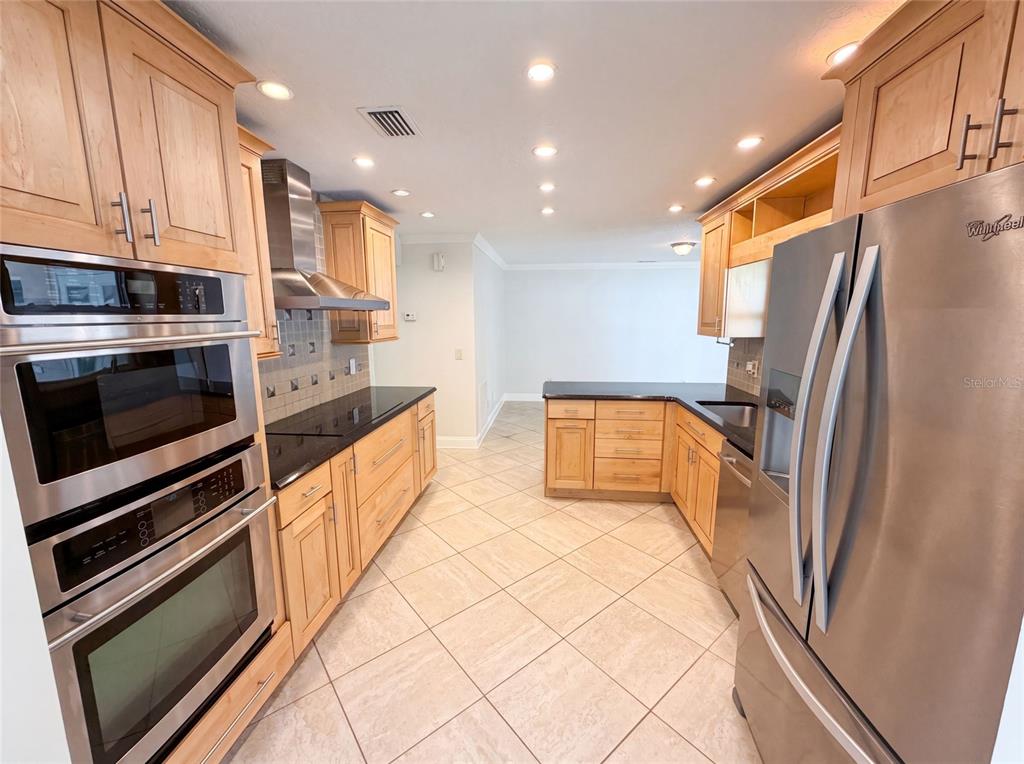 A kitchen features light wood cabinets, stainless steel appliances, black countertops, and light tile flooring — 2223 CONIFER AVENUE, WINTER PARK, FL
