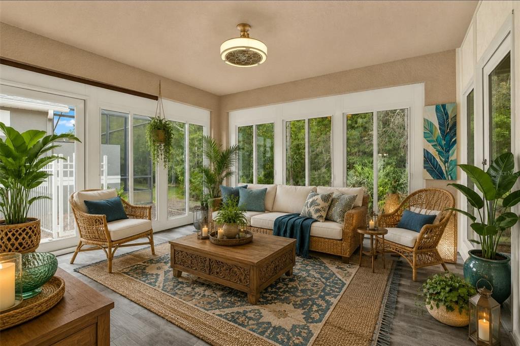 A sunroom with wicker furniture, a patterned rug, and large windows overlooking a wooded area — 21054 DIAMONTE DR, LAND O LAKES, FL