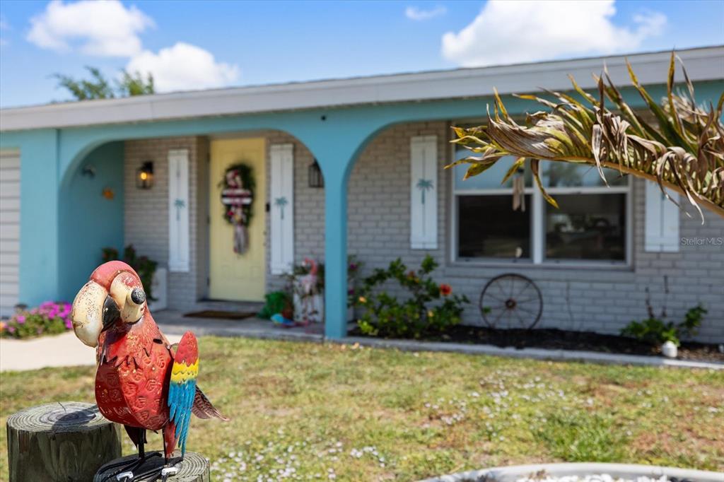 A metal parrot statue sits in the foreground of a house with a yellow door — 168 BUCKEYE AVENUE NW, PORT CHARLOTTE, FL