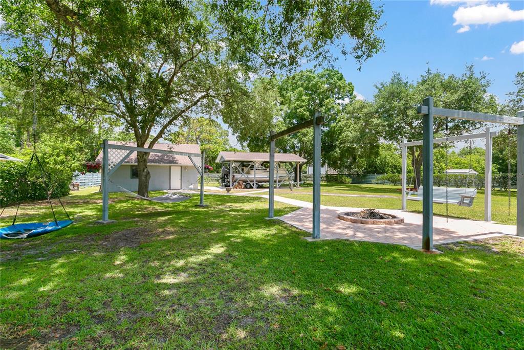 A grassy backyard features a fire pit, a swing set, a hammock, and a boat shelter — 4970 PINEWOOD PLACE, COCOA, FL
