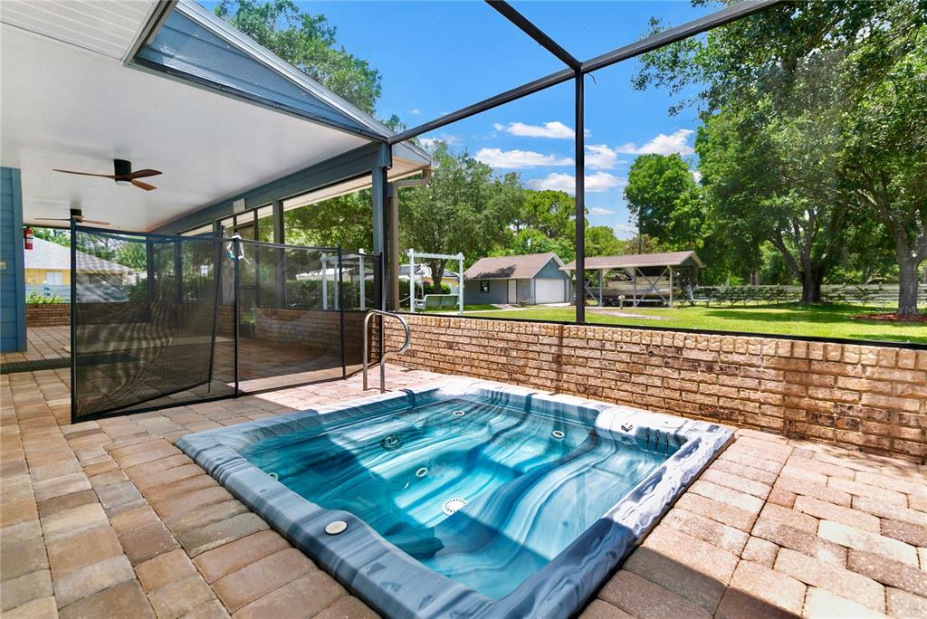 A hot tub sits on a brick patio inside a screened-in lanai overlooking a yard — 4970 PINEWOOD PLACE, COCOA, FL