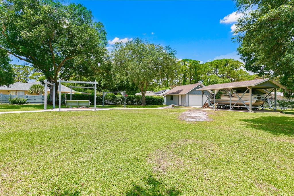 A grassy backyard features a swing set, a hammock, a detached garage, and a boat shelter — 4970 PINEWOOD PLACE, COCOA, FL