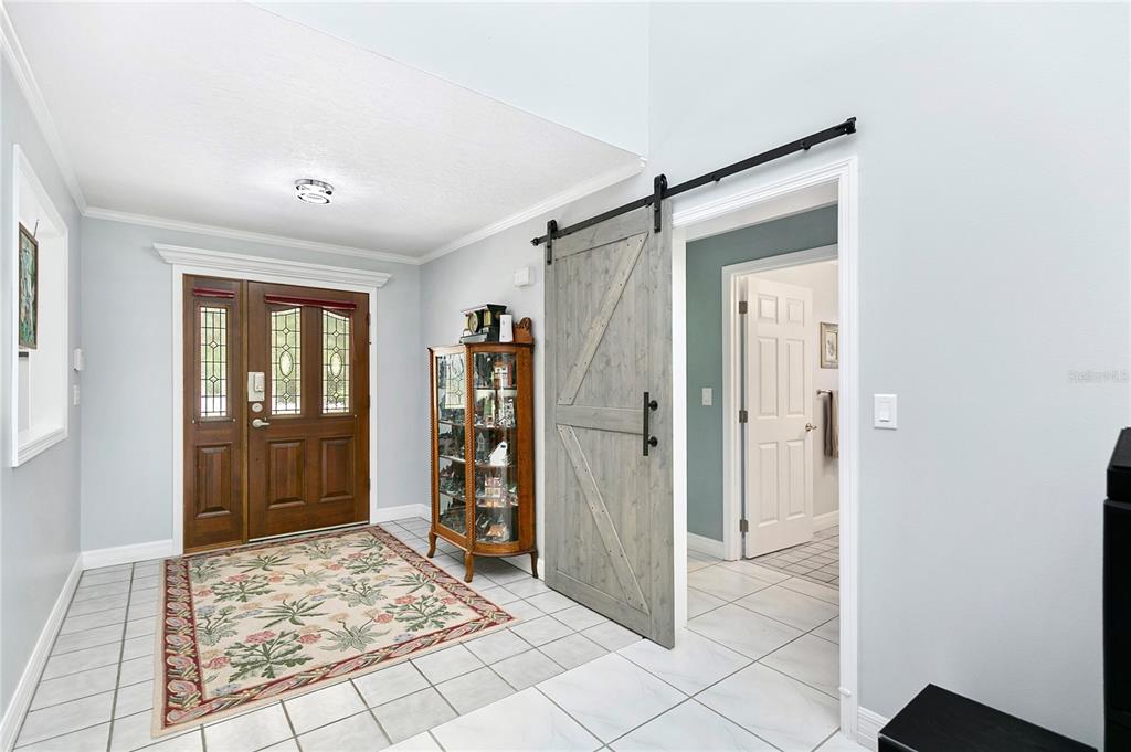 An entryway features a wood front door, a glass display cabinet, and a sliding barn door — 4970 PINEWOOD PLACE, COCOA, FL
