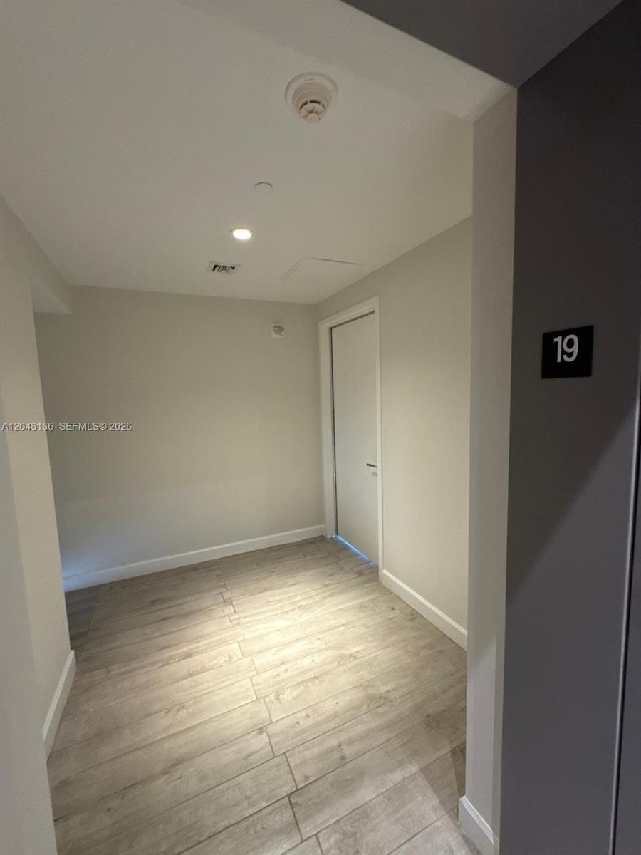 A hallway with light-colored wood-look flooring leads to a closed white door — 460 NE 28th St # 1907, Miami FL 33137, MIAMI, FL