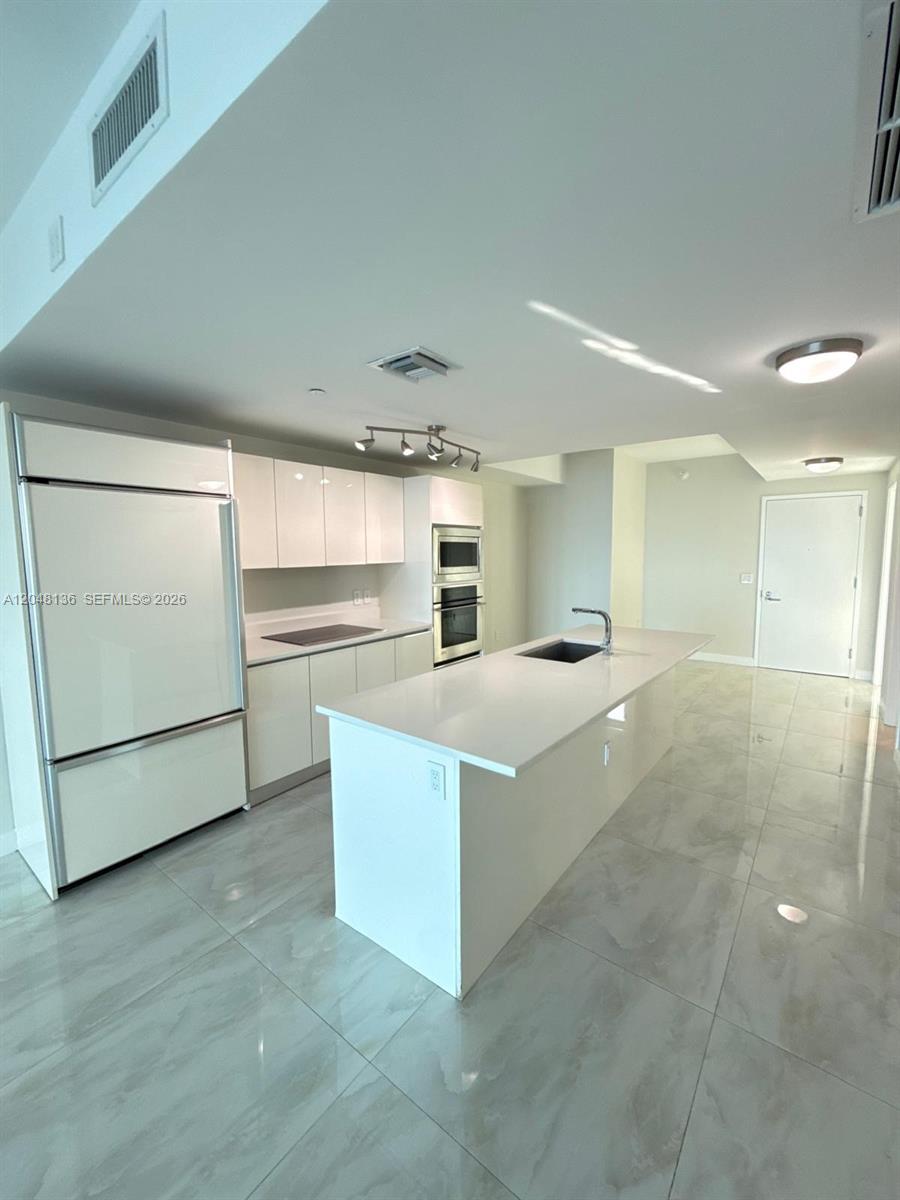 A modern kitchen features white cabinetry, a central island with a sink, and tiled flooring — 460 NE 28th St # 1907, Miami FL 33137, MIAMI, FL