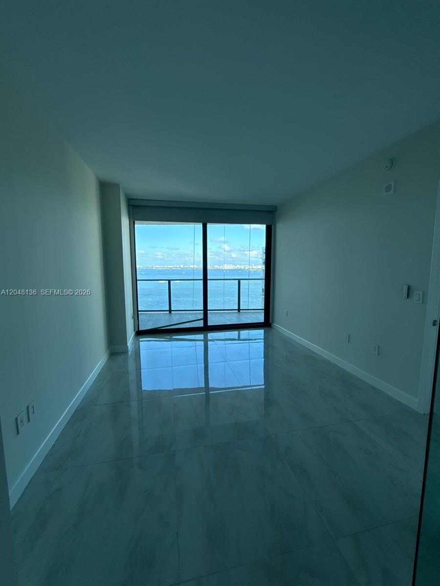 An empty room with light-colored tile flooring and a sliding glass door overlooking the ocean — 460 NE 28th St # 1907, Miami FL 33137, MIAMI, FL