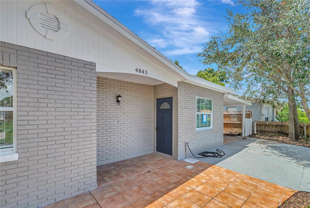 A gray brick house features a tiled front porch and a dark blue front door — 4845 SAN PABLO PLACE, TAMPA, FL