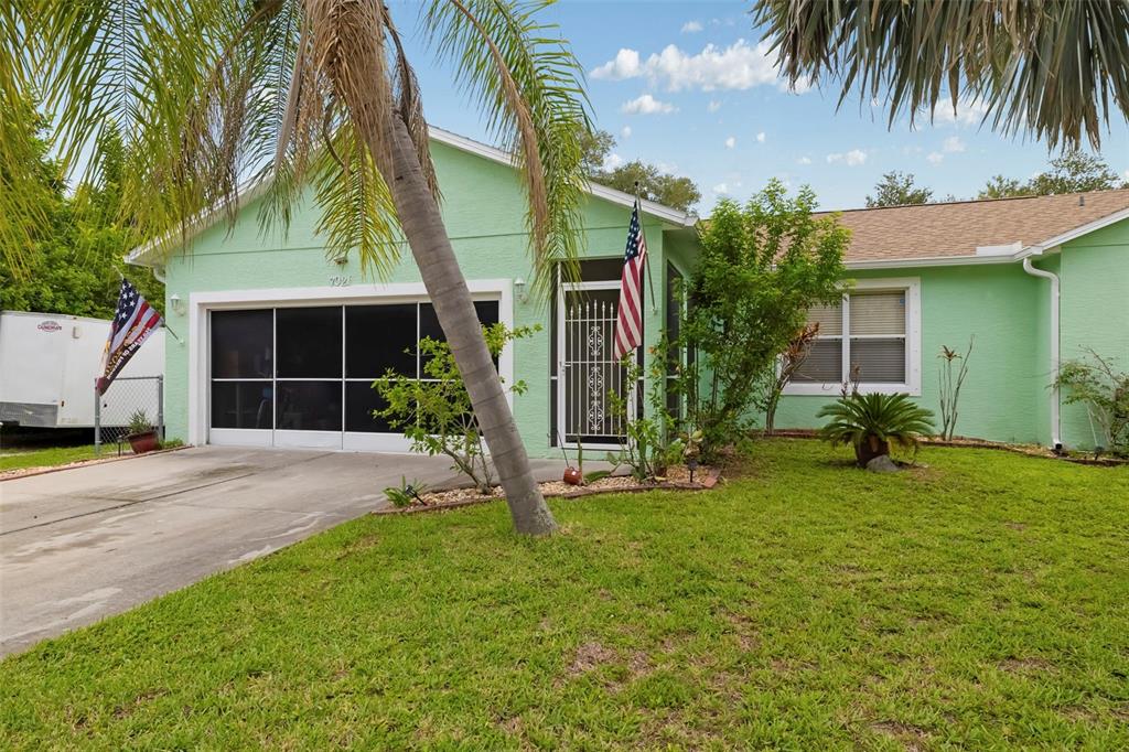 A light green single-story house features a screened garage, a front porch, and a lawn — 7021 FANCY STREET, ENGLEWOOD, FL