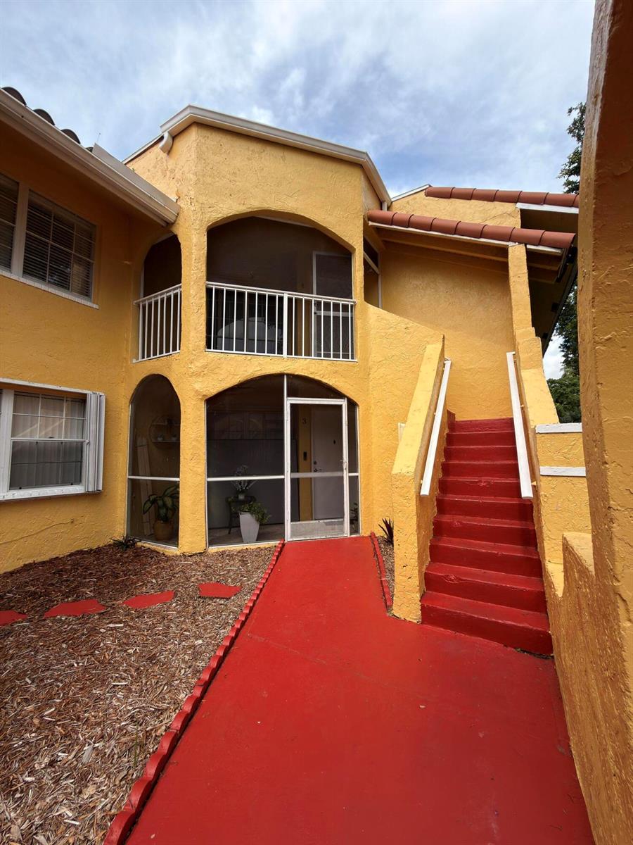 Exterior view of a yellow two-story building with a red staircase and screened-in porches — 15605 SW 74th Cir Drive # 4, Miami FL 33193, MIAMI, FL