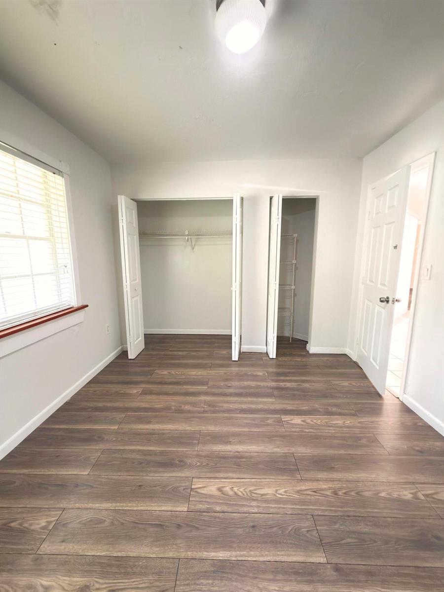 An empty bedroom features wood-look flooring, white walls, a window, and two open closets — 15605 SW 74th Cir Drive # 4, Miami FL 33193, MIAMI, FL