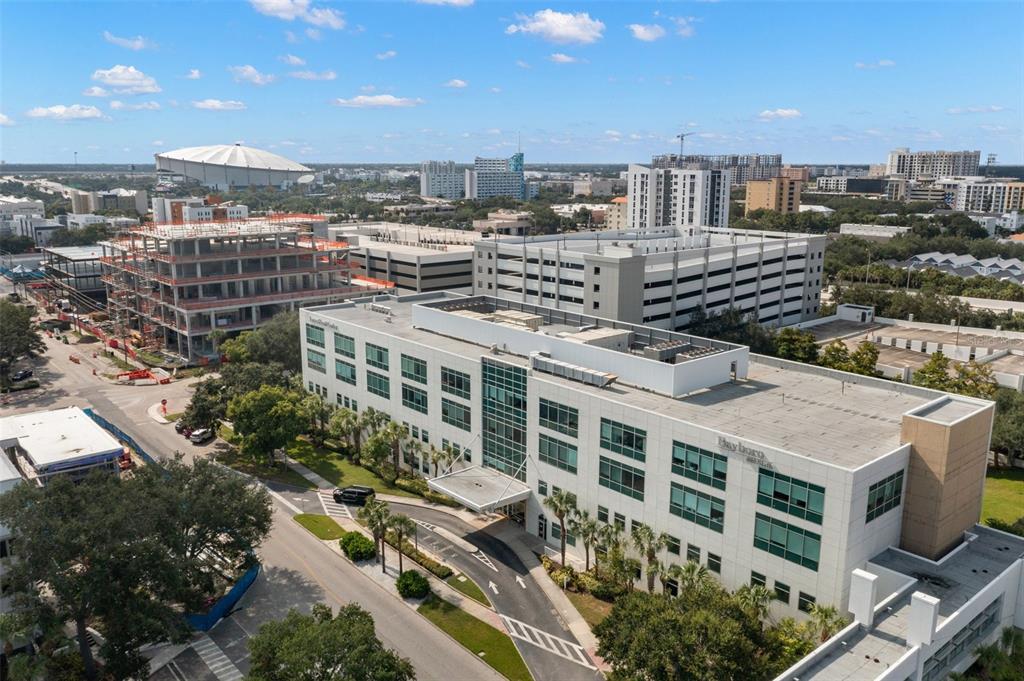 An aerial view shows a multi-story office building with a parking garage and construction site — 625 6TH AVENUE S UNIT 405, ST PETERSBURG, FL
