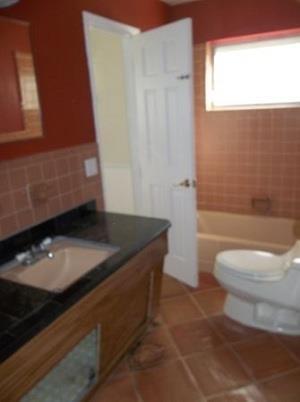 A bathroom with a wooden vanity, black countertop, terracotta-colored walls, and a white toilet — 223 SE 14th Place, Deerfield Beach FL 33441, DEERFIELD BEACH, FL