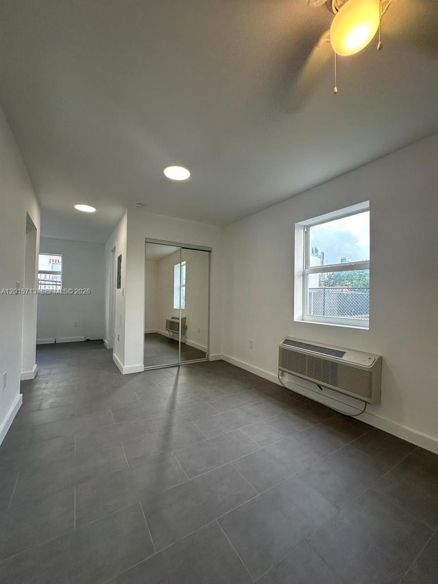 A bedroom features gray tile flooring, white walls, a mirrored closet, and a wall-mounted AC unit — 1535 NW 1st Pl # 10, Miami FL 33136, MIAMI, FL