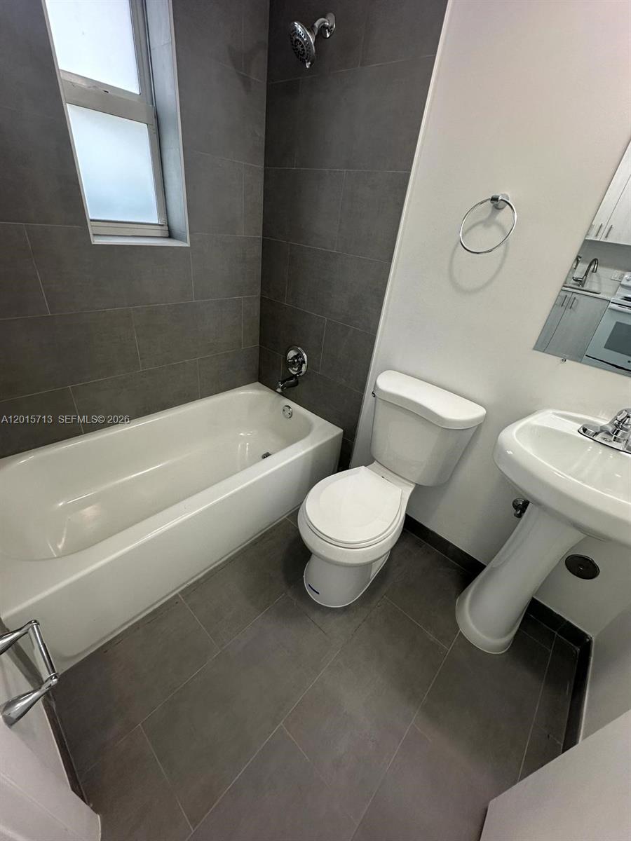 A bathroom features a white tub, a pedestal sink, and gray tiled flooring and walls — 1535 NW 1st Pl # 10, Miami FL 33136, MIAMI, FL