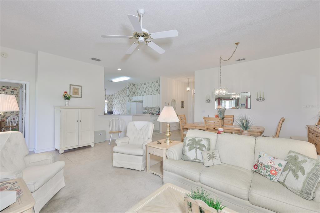 A living room with a ceiling fan, beige carpet, and an adjacent dining area — 2308 BROOKFIELD GREENS CIRCLE, SUN CITY CENTER, FL