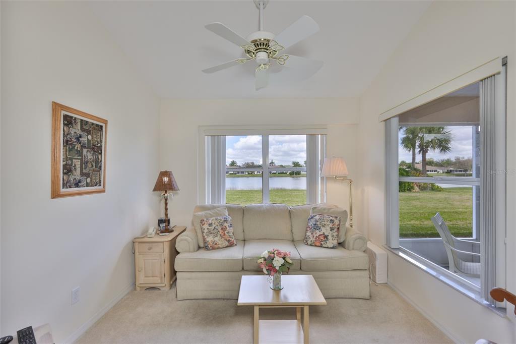 A living room features a beige sofa, a coffee table, and windows overlooking a lake — 2308 BROOKFIELD GREENS CIRCLE, SUN CITY CENTER, FL