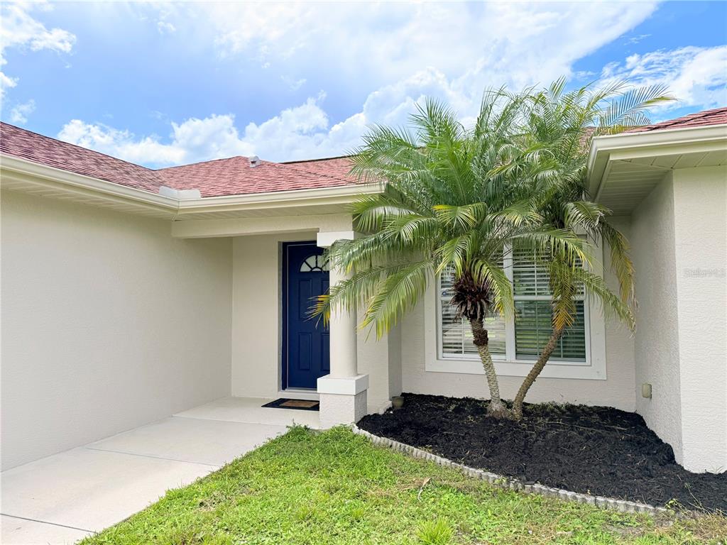 The exterior of a house features a blue front door, a palm tree, and landscaping — 4143 DANBURY TERRACE, NORTH PORT, FL
