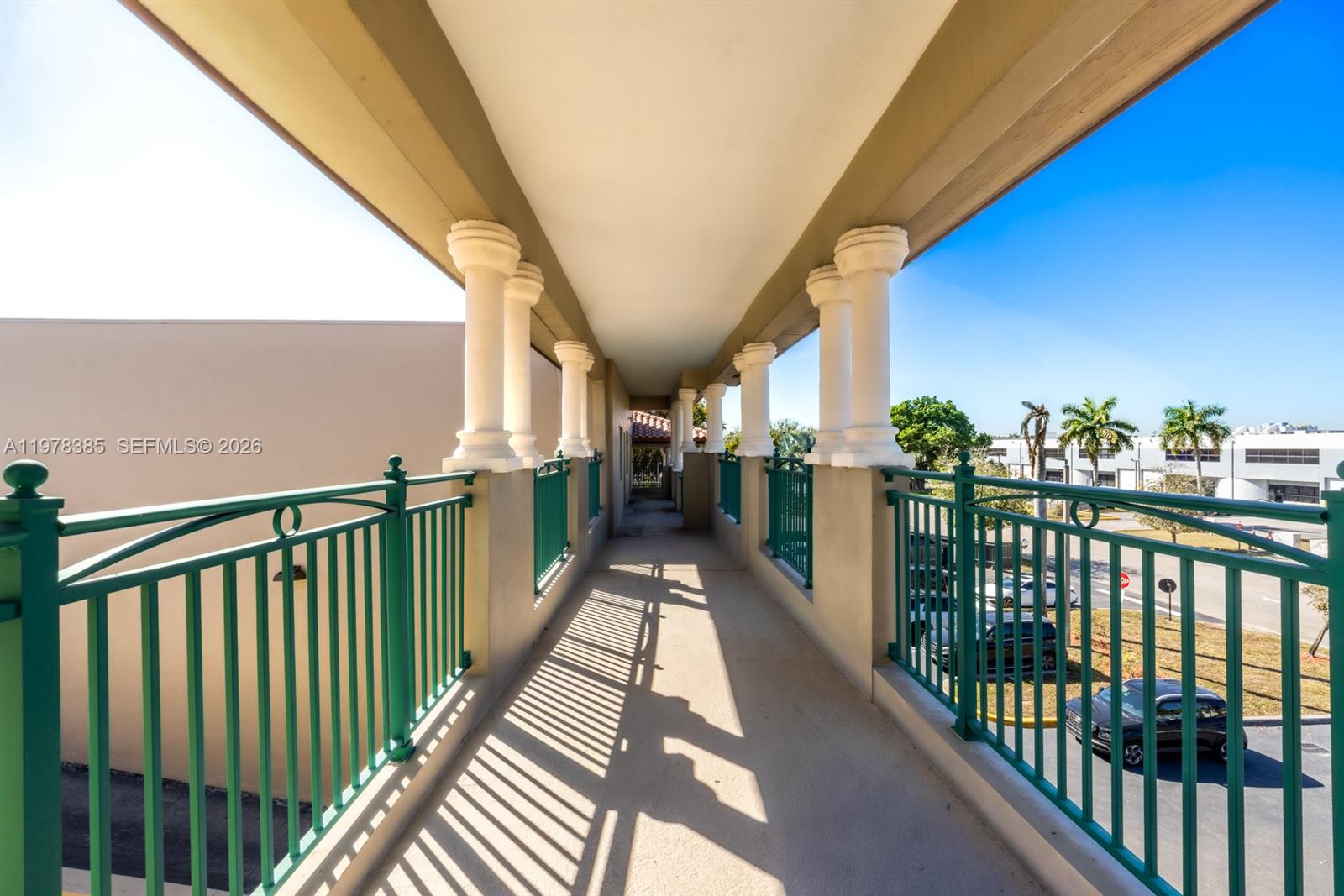 An outdoor covered walkway features green metal railings and white columns under a clear sky — 10200 NW 25th St, Doral FL 33172, DORAL, FL