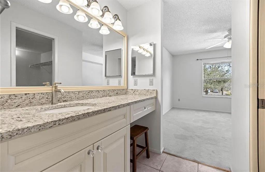 A bathroom with a granite vanity and mirror leads into a carpeted bedroom with a window — 7294 CLOISTER DRIVE UNIT 23, SARASOTA, FL