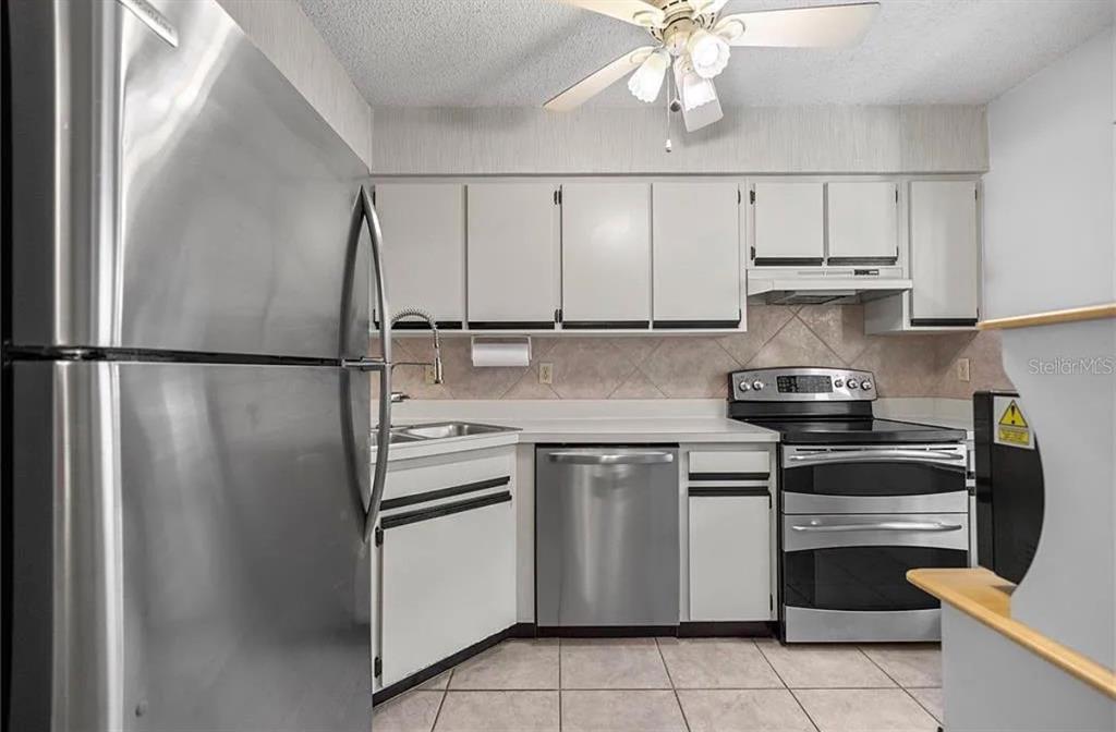 A kitchen features stainless steel appliances, white cabinets, and light-colored tile flooring — 7294 CLOISTER DRIVE UNIT 23, SARASOTA, FL