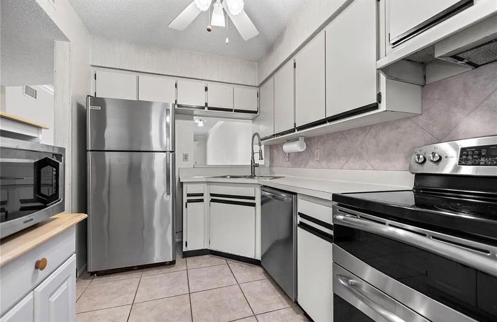 A kitchen with white cabinets, stainless steel appliances, tile flooring, and a pass-through window — 7294 CLOISTER DRIVE UNIT 23, SARASOTA, FL