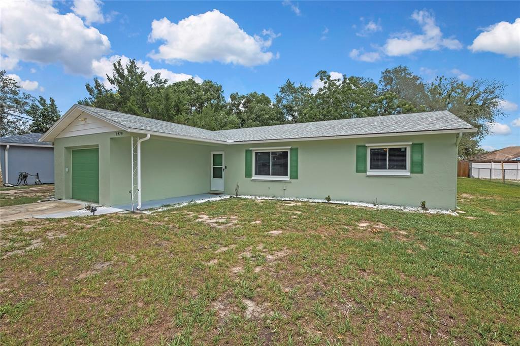 A light green single-story house with a garage and green shutters under a cloudy sky — 9279 PICKENS STREET, SPRING HILL, FL