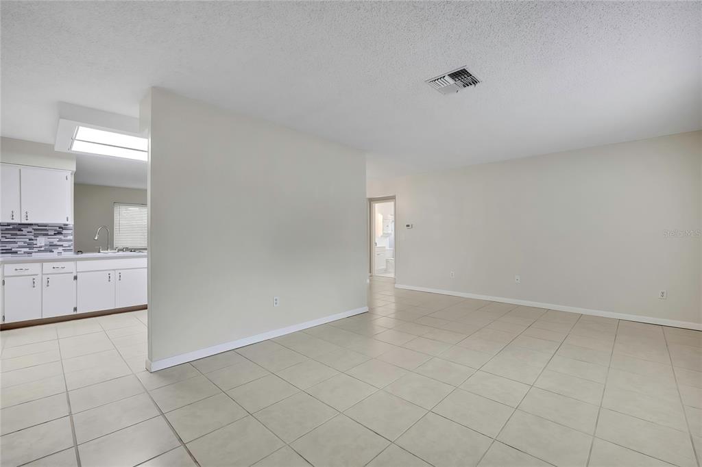 An open-concept living area with light-colored tile flooring leads into a kitchen with white cabinets — 9279 PICKENS STREET, SPRING HILL, FL