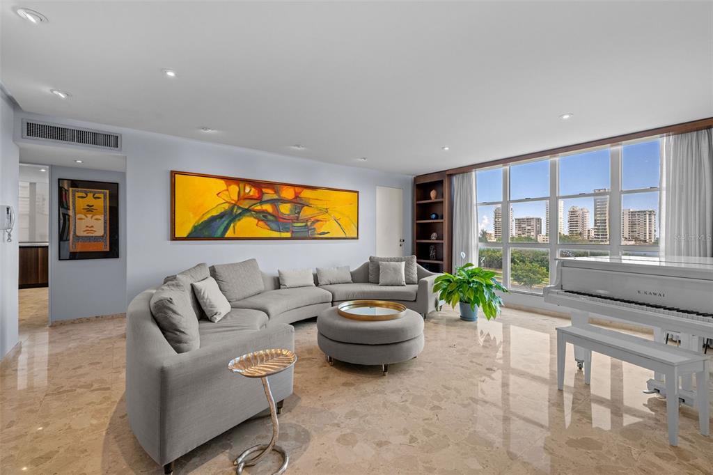 A living room features a curved gray sectional, a white piano, and large floor-to-ceiling windows — 548 Hoare St. LAGUNA UNIT 3, SAN JUAN, PR