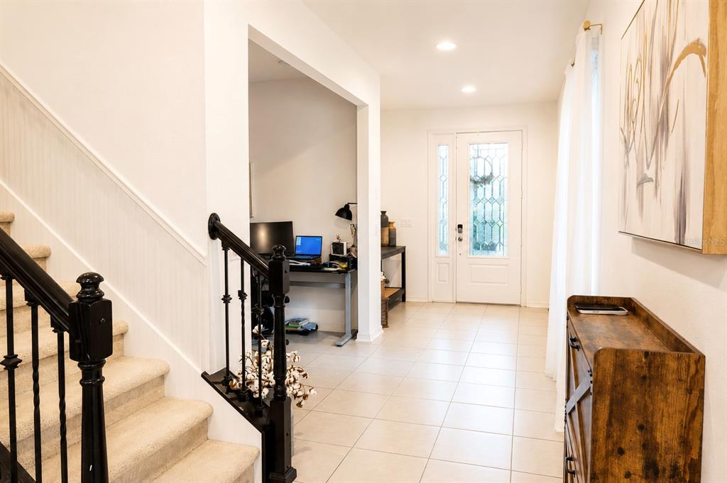 An entryway features a staircase with black railings, tiled floors, and an adjacent home office — 8205 BAYLISS COURT, ORLANDO, FL