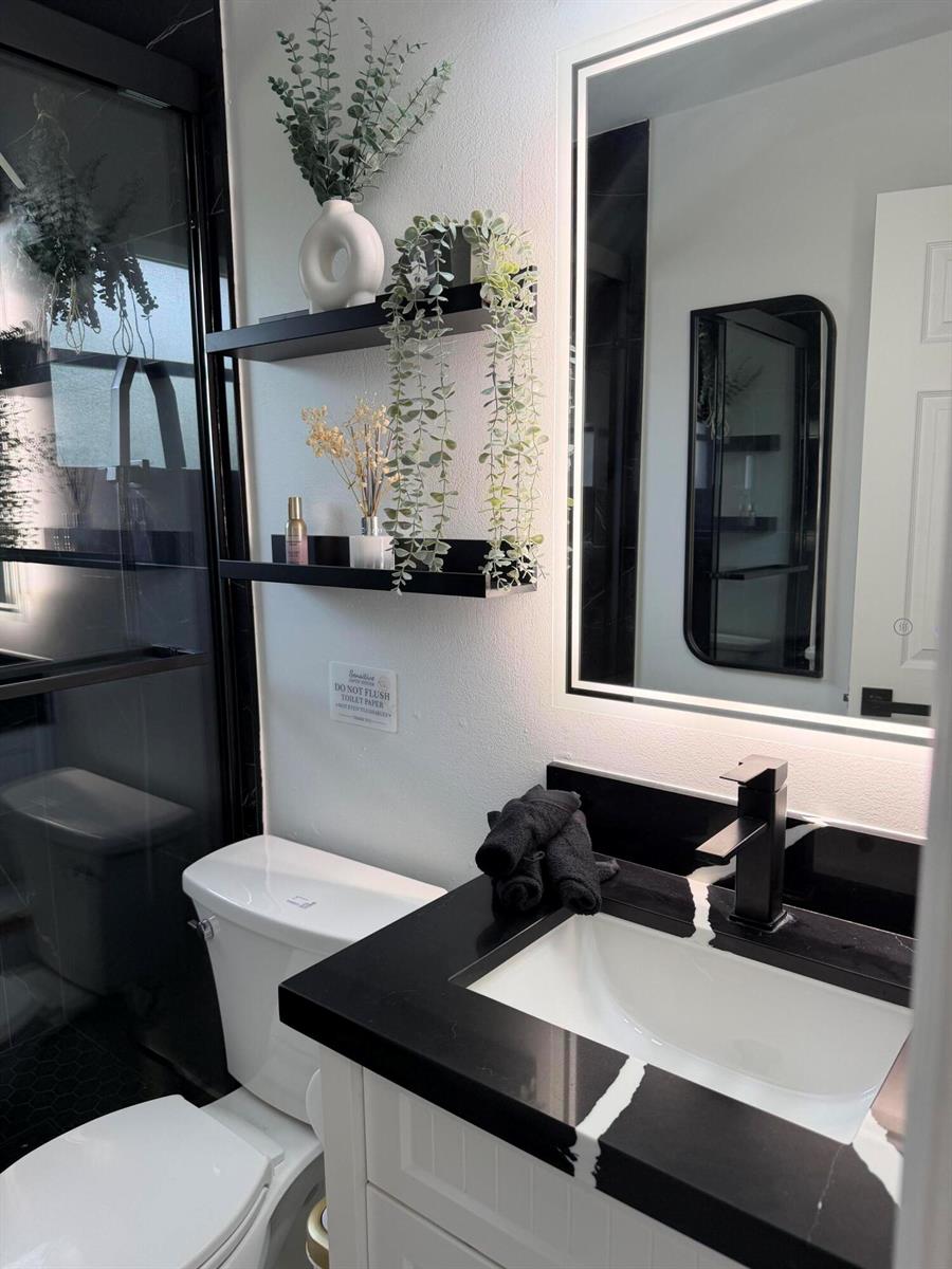 A modern bathroom features a black-and-white vanity, floating shelves with greenery, and a lighted mirror — 9052 Fountain Road, Lake Worth FL 33467, LAKE WORTH, FL