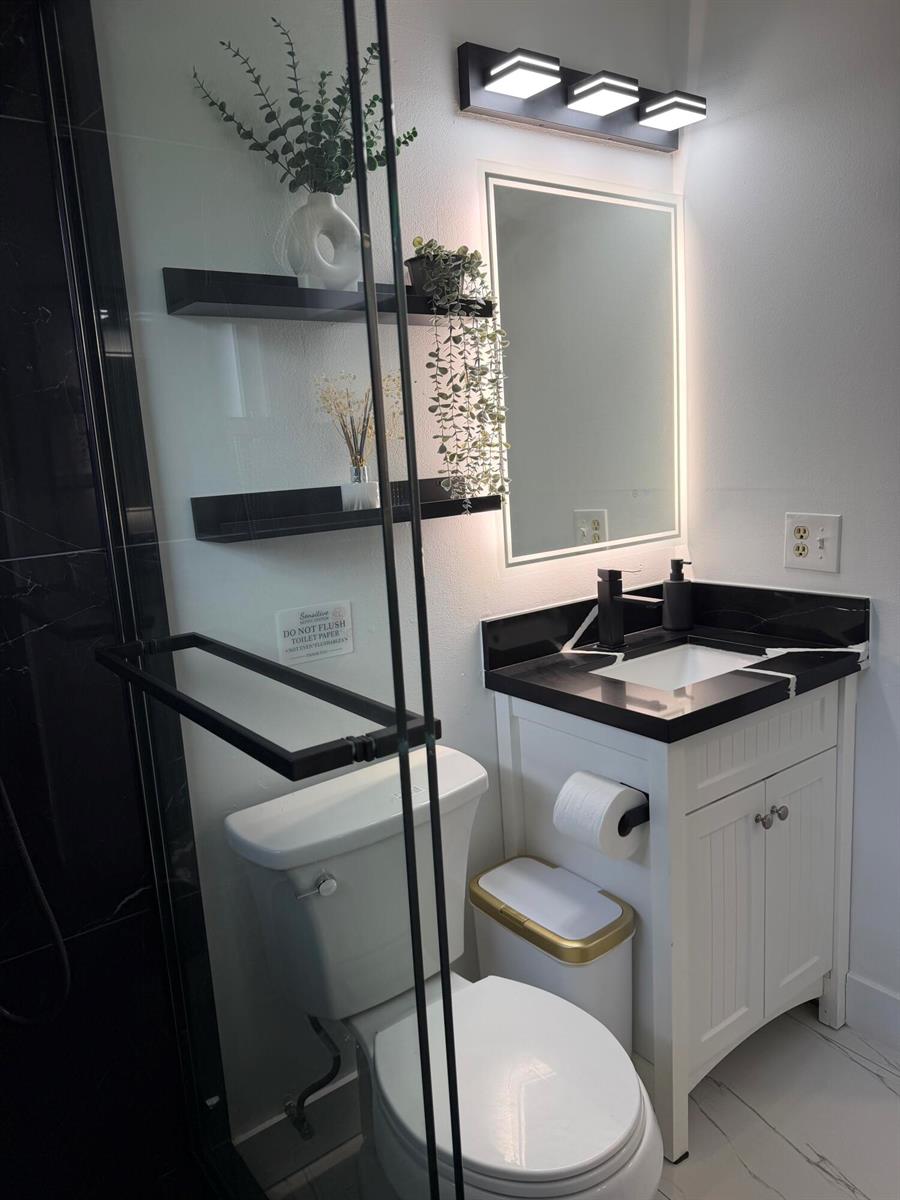 A modern bathroom features a white vanity with a black countertop, toilet, and floating shelves — 9052 Fountain Road, Lake Worth FL 33467, LAKE WORTH, FL