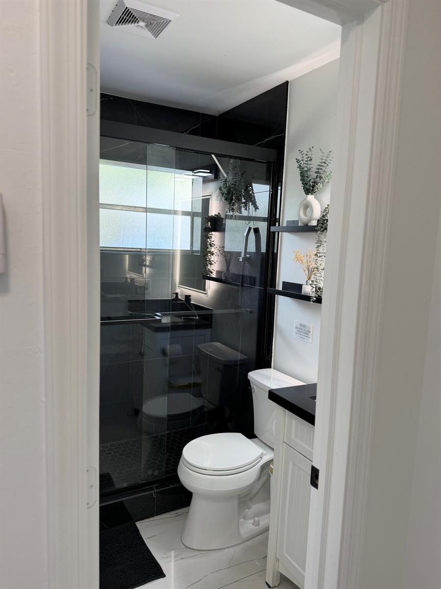 A bathroom features a glass-enclosed shower, a white toilet, and black floating shelves — 9052 Fountain Road, Lake Worth FL 33467, LAKE WORTH, FL