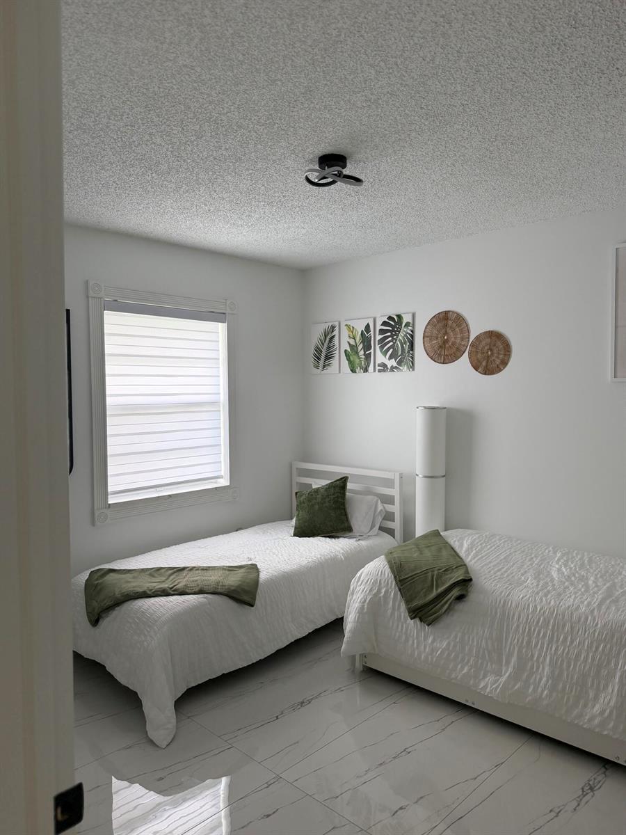 A bedroom with two twin beds, white bedding, green accents, and white marble-look tile flooring — 9052 Fountain Road, Lake Worth FL 33467, LAKE WORTH, FL