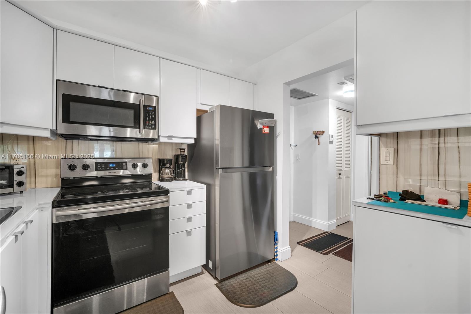 A kitchen features white cabinets, stainless steel appliances, and light-colored tile flooring — 257 S Cypress Rd # 416, Pompano Beach FL 33060, POMPANO BEACH, FL