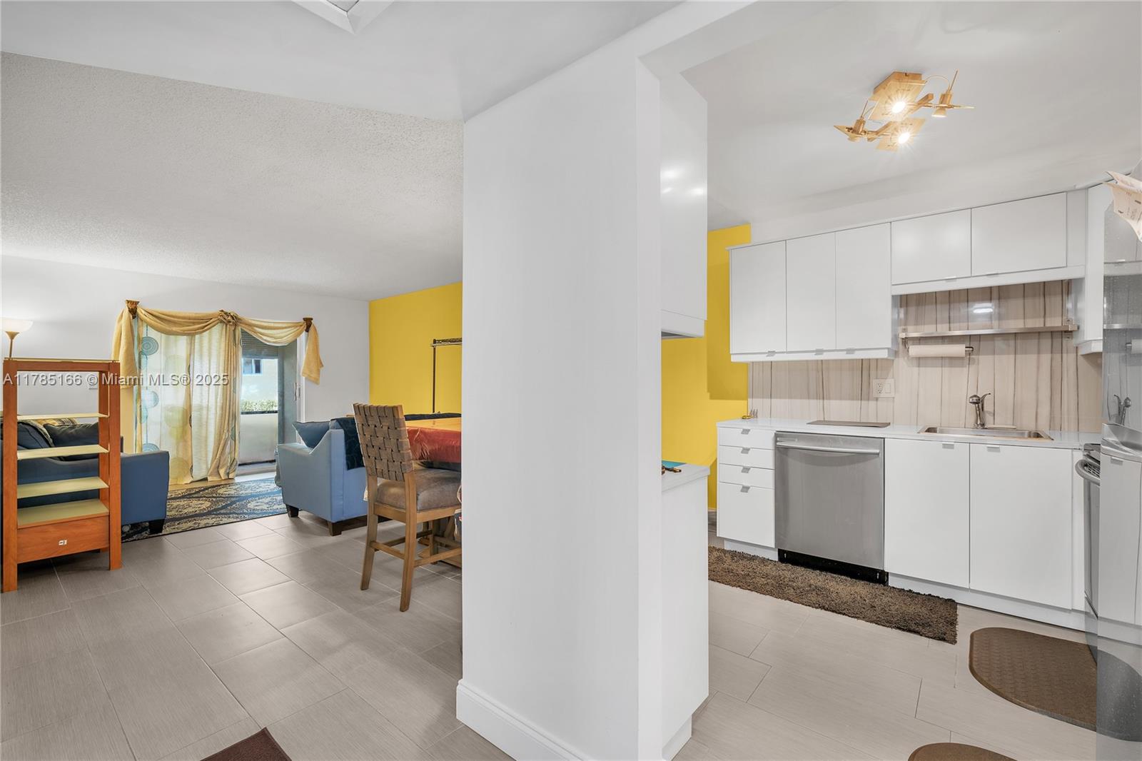 An open-concept kitchen with white cabinets and stainless steel appliances overlooks a living area — 257 S Cypress Rd # 416, Pompano Beach FL 33060, POMPANO BEACH, FL