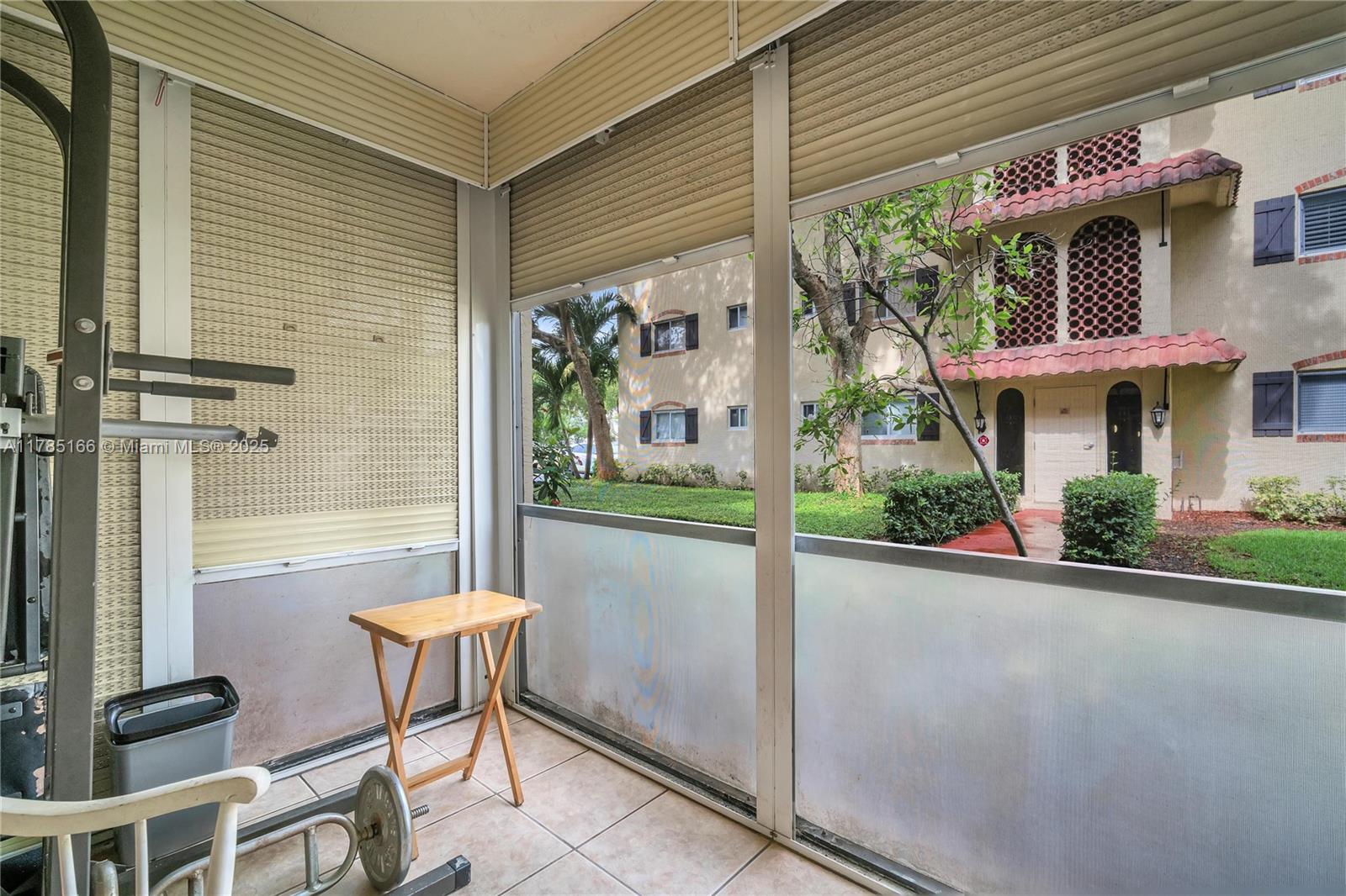 A tiled balcony with exercise equipment and a folding table overlooks a neighboring apartment building — 257 S Cypress Rd # 416, Pompano Beach FL 33060, POMPANO BEACH, FL