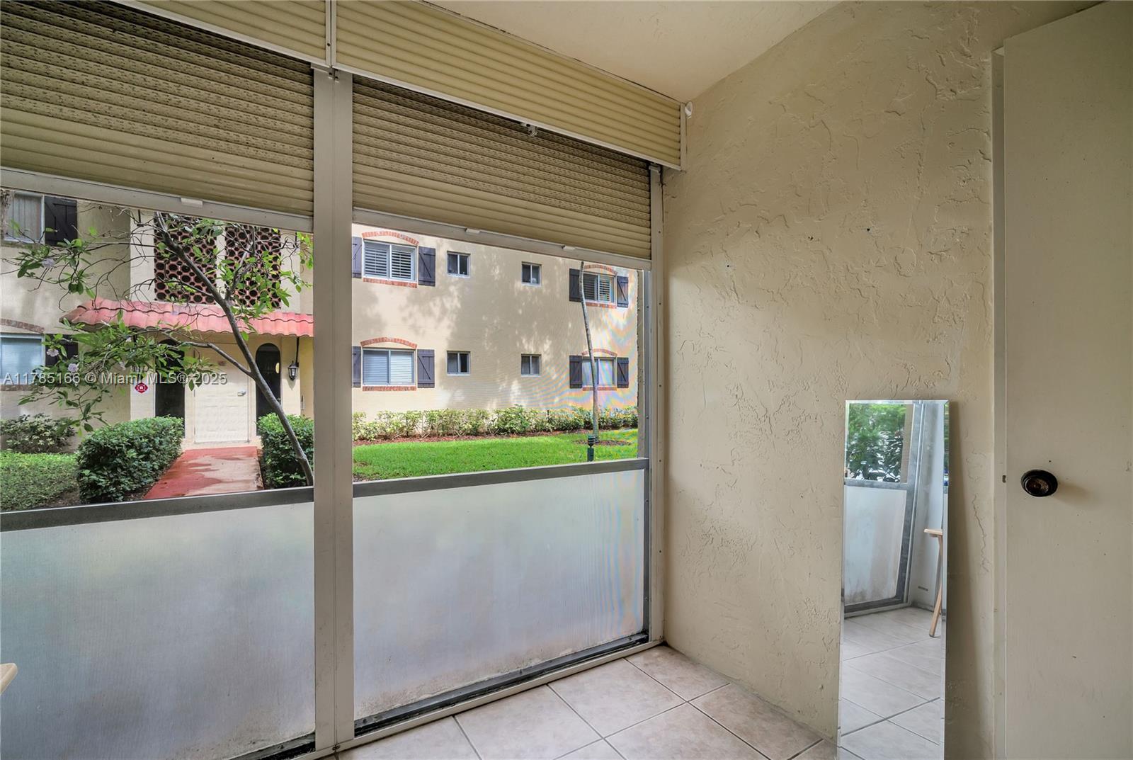 A sunroom features tiled floors, a large window with blinds, and a leaning floor mirror — 257 S Cypress Rd # 416, Pompano Beach FL 33060, POMPANO BEACH, FL