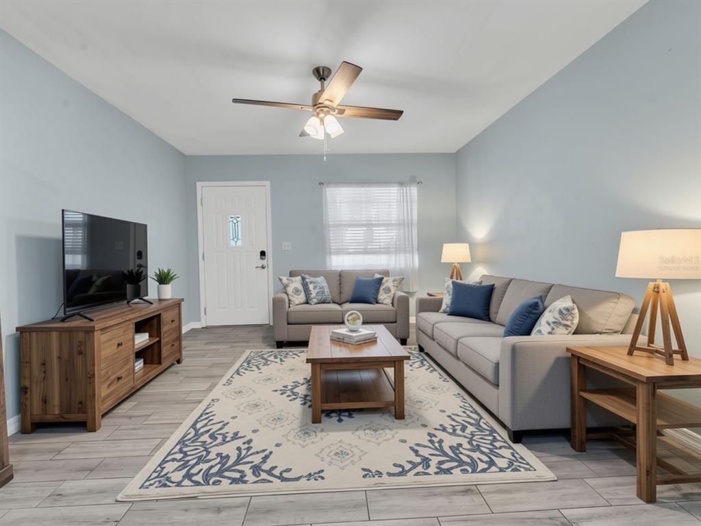 A living room features light blue walls, gray tile flooring, a ceiling fan, and furniture — 1966 MCKINLEY STREET, CLEARWATER, FL