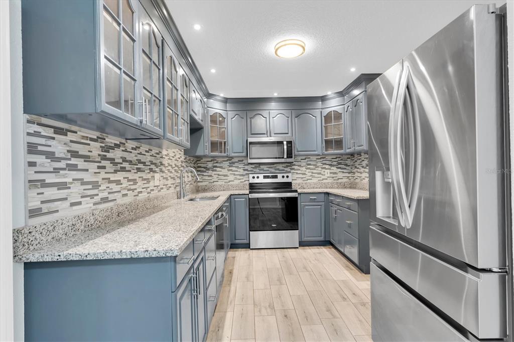 A kitchen features blue cabinets, granite countertops, stainless steel appliances, and a tiled backsplash — 1966 MCKINLEY STREET, CLEARWATER, FL