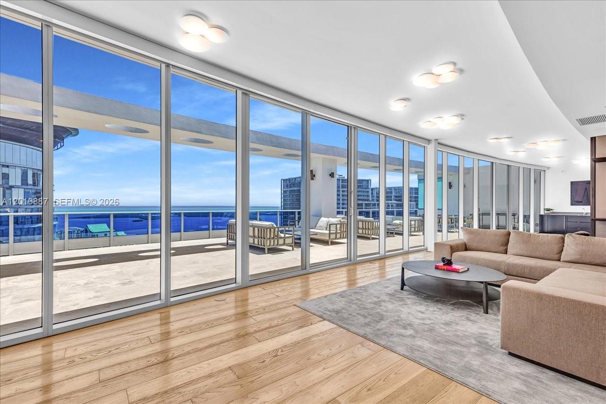 A living room features floor-to-ceiling glass walls opening onto a balcony with ocean views — 200 Biscayne Boulevard Way # 5401, Miami FL 33131, MIAMI, FL