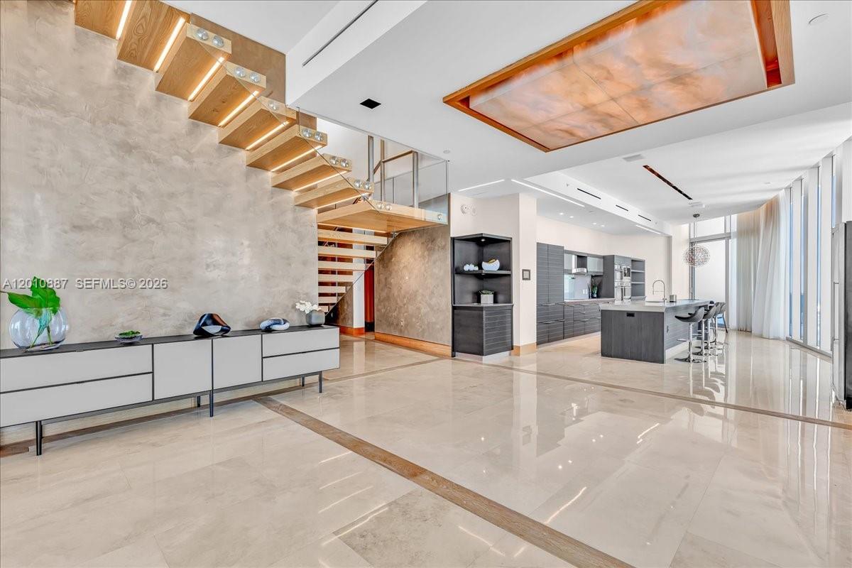 A modern, open-concept living area features a floating wooden staircase and a sleek kitchen — 200 Biscayne Boulevard Way # 5401, Miami FL 33131, MIAMI, FL