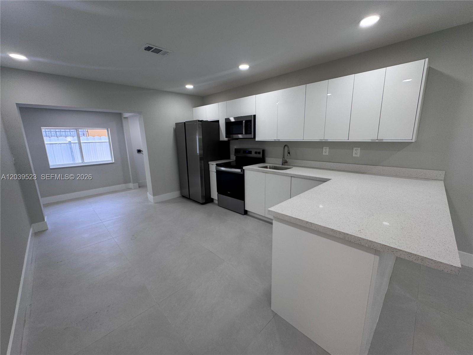 A modern kitchen features white flat-panel cabinets, stainless steel appliances, and light-colored quartz countertops — 850 NW 109th St # 852, Miami FL 33168, MIAMI, FL
