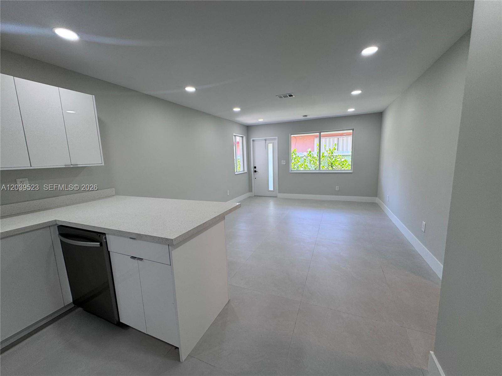 A modern kitchen with white cabinets and a gray countertop opens into a living area — 850 NW 109th St # 852, Miami FL 33168, MIAMI, FL